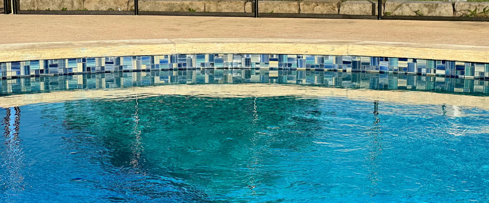 Close-up of new blue mosaic waterline tile and stone coping from a pool renovation in Round Rock
